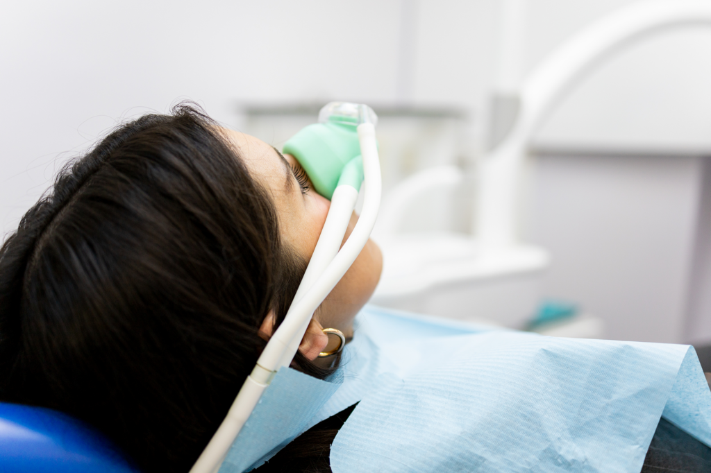 A patient reclines in a dental chair wearing a nasal mask to receive nitrous oxide sedation before or during a dental procedure.