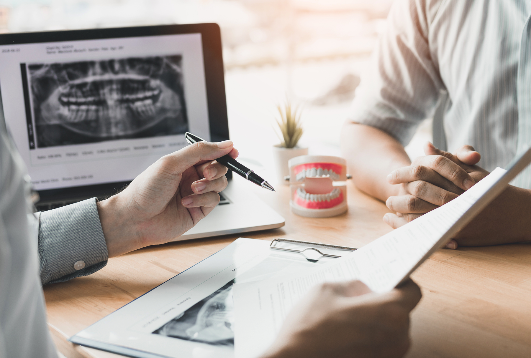 A dental professional reviews a patient's dental X-ray and treatment plan with a patient before an oral surgery consultation.