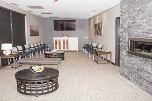Dental waiting room with rows of chairs, central coffee table, stone fireplace, and TV mounted on wall