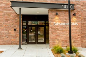 Entrance to “Advanced OMS” at 1010, brick facade, glass doors, landscaping, pole-mounted sign
