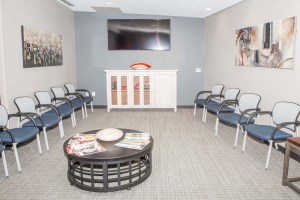 Symmetrical waiting area: blue chairs, white cabinet, wall art, and round coffee table with magazines