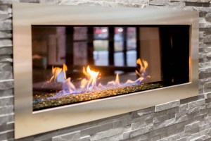 Modern linear gas fireplace with flames over glass beads, stainless steel frame, stone surround