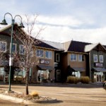 Multi-tenant commercial building with brown/green siding, gabled roofs, storefronts, and black SUV parked front