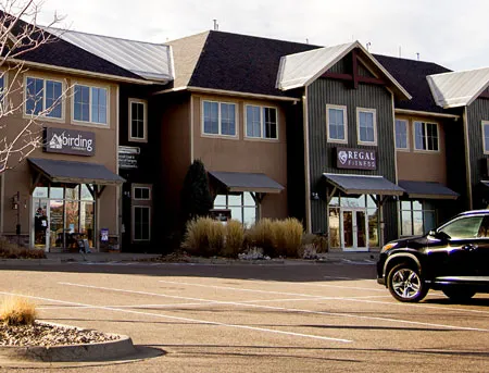 Multi-tenant retail/office building with “Savings” and “RETAIL” signs, SUV parked front