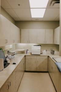 Dental lab/sterilization room: U-shaped beige cabinetry, autoclave, sink, and overhead fluorescent lighting
