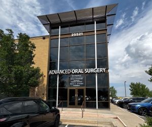 Modern glass-front building with “ADVANCED ORAL SURGERY” signage, address 29521, parked cars, trees